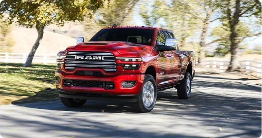 Red 2026 Ram 2500 Heavy Duty pickup driving along a tree-lined road